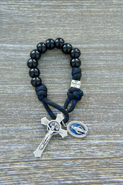 The Solemn Crusader - Blue Black and Silver 1 Decade Paracord Rosary: A durable and unbreakable premium paracord rosary, perfect for young Catholics on their spiritual journey. This kid-friendly Catholic gift features black paracord, shiny black Hail Mary beads, silver crusader Our Father beads, a 2" silver St. Benedict crucifix, and an attached blue enamel 1" Miraculous Medal.
