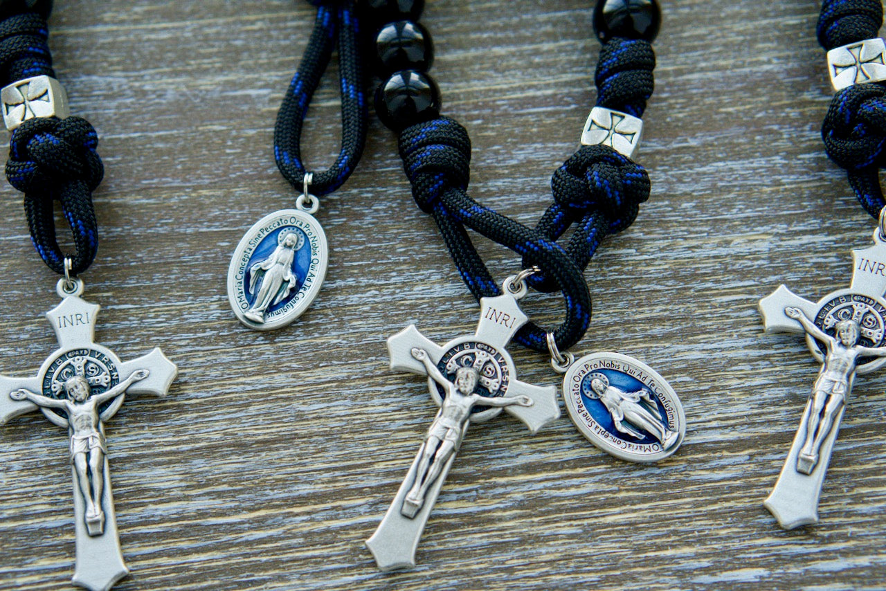 The Solemn Crusader - Blue Black and Silver 1 Decade Paracord Rosary: A premium unbreakable paracord rosary crafted with solemnity and devotion, featuring black paracord, 12mm shiny black Hail Mary beads, silver crusader Our Father beads, a silver St. Benedict crucifix, and a blue enamel Miraculous Medal.