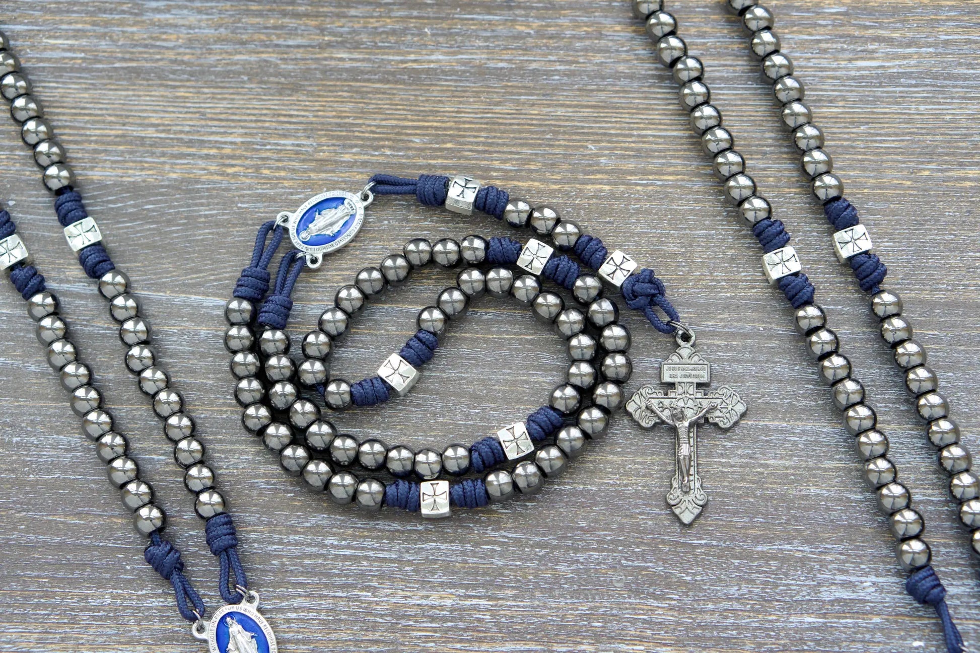 Silver crusader Our Father beads and gunmetal Hail Mary beads adorn The Solemn Crusader metal paracord rosary, featuring a blue enamel Miraculous Medal centerpiece.