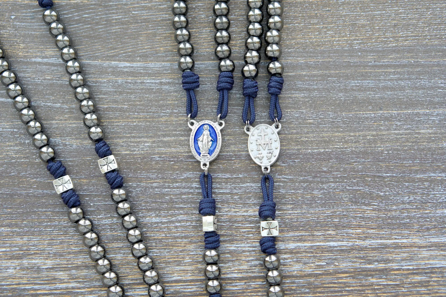 The Solemn Crusader: navy blue paracord rosary with silver crusader Our Father beads, gunmetal Hail Mary beads, and a blue enamel Miraculous Medal centerpiece.