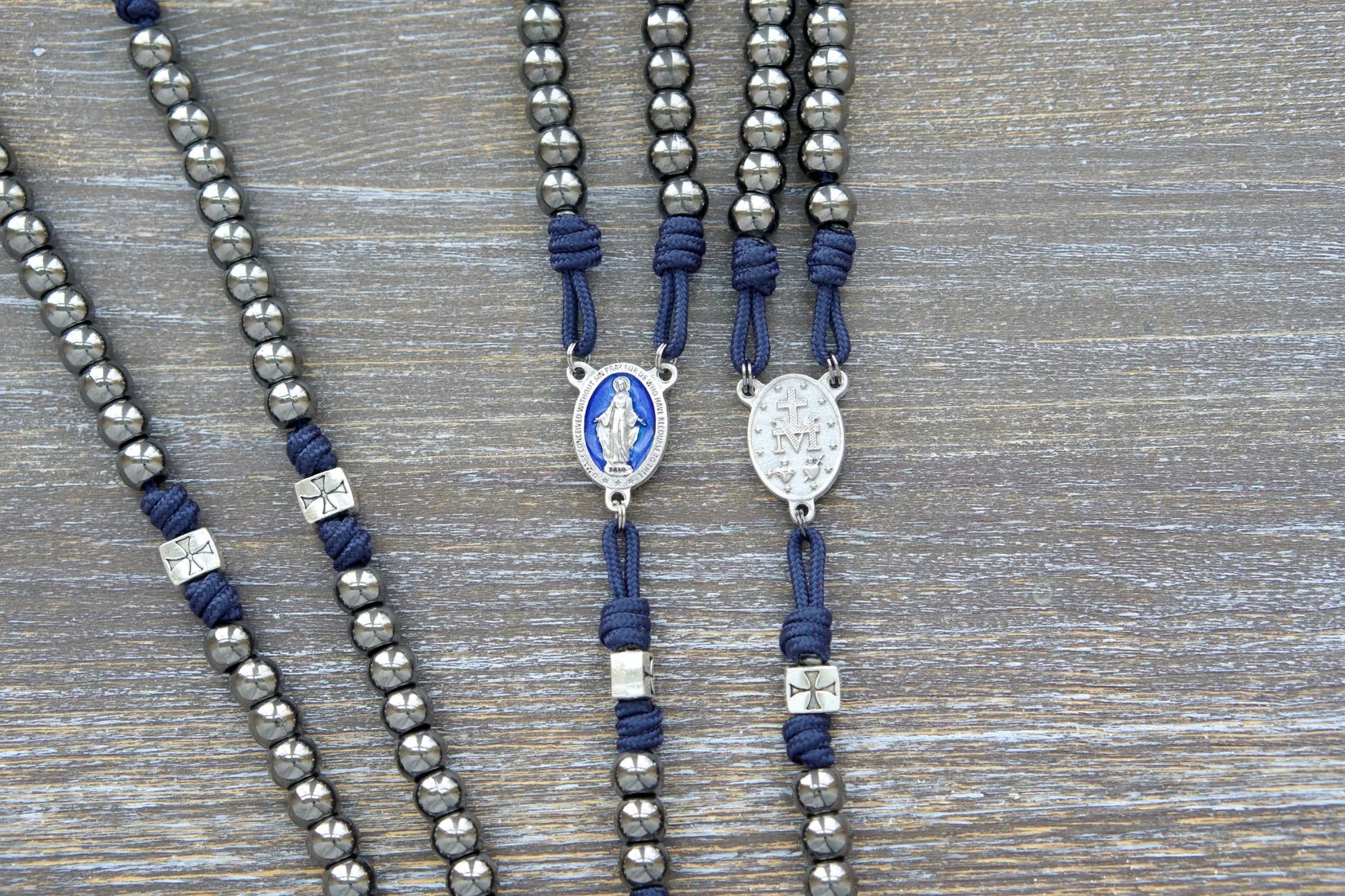 The Solemn Crusader: navy blue paracord rosary with silver crusader Our Father beads, gunmetal Hail Mary beads, and a blue enamel Miraculous Medal centerpiece.