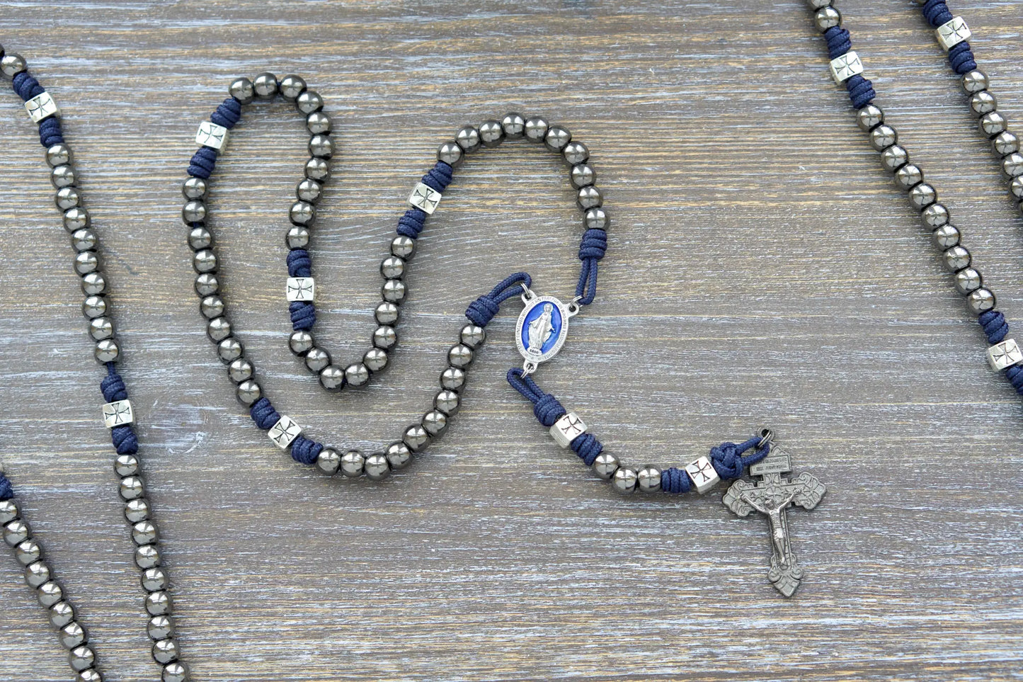 Metal paracord rosary, The Solemn Crusader, features navy blue paracord, silver crusader Our Father beads, gunmetal Hail Mary beads, and a blue enamel Miraculous Medal centerpiece.