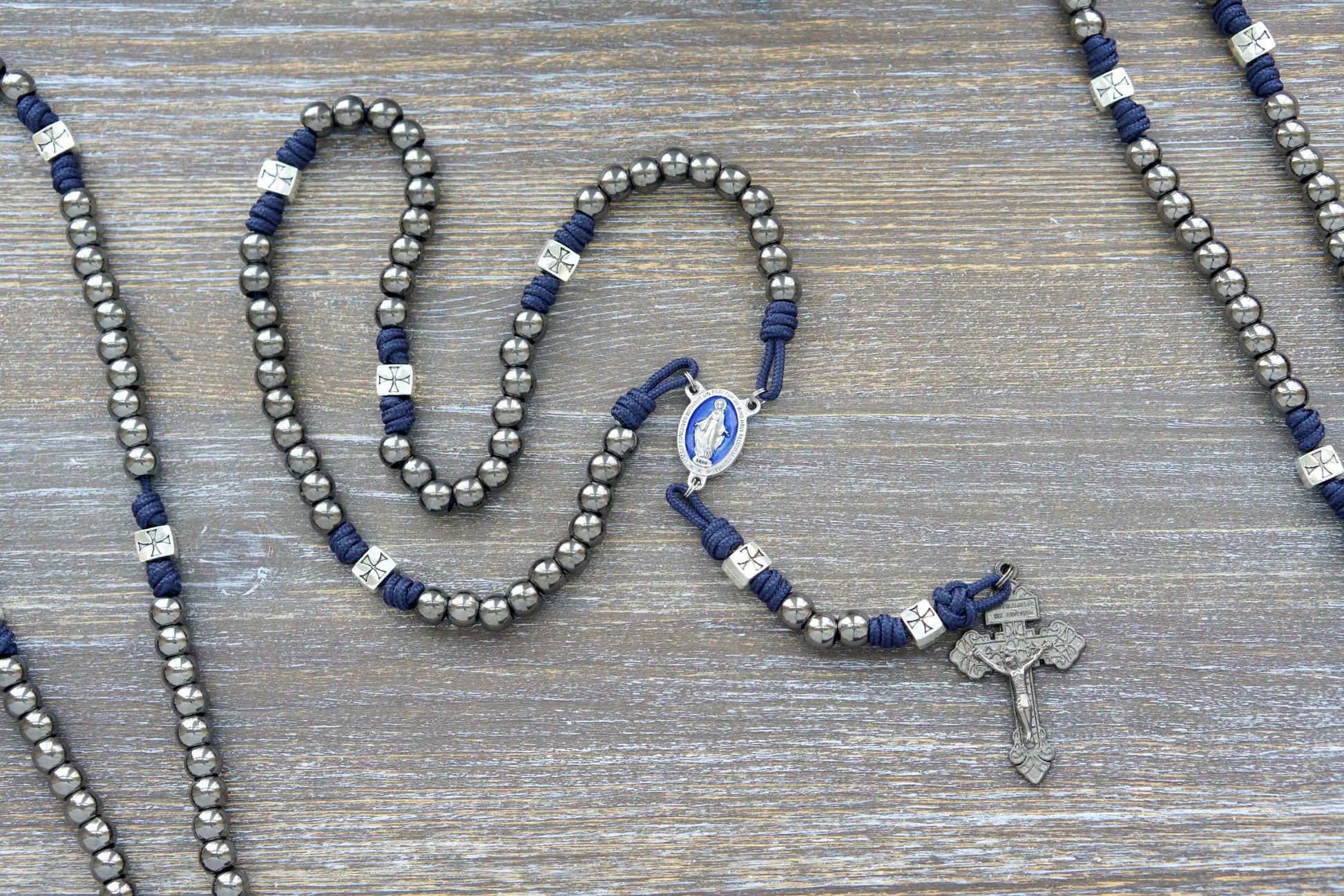 Metal paracord rosary, The Solemn Crusader, features navy blue paracord, silver crusader Our Father beads, gunmetal Hail Mary beads, and a blue enamel Miraculous Medal centerpiece.