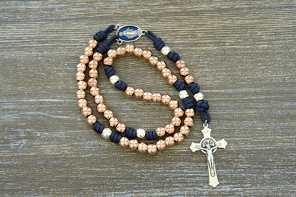 Beautiful rose gold and navy blue paracord rosary with durable, premium design and elegant blue enamel Our Lady of the Miraculous Medal centerpiece - perfect for strong Catholic women who want to stand out in faith. Splendor of the Stars by Sanctus Servo.