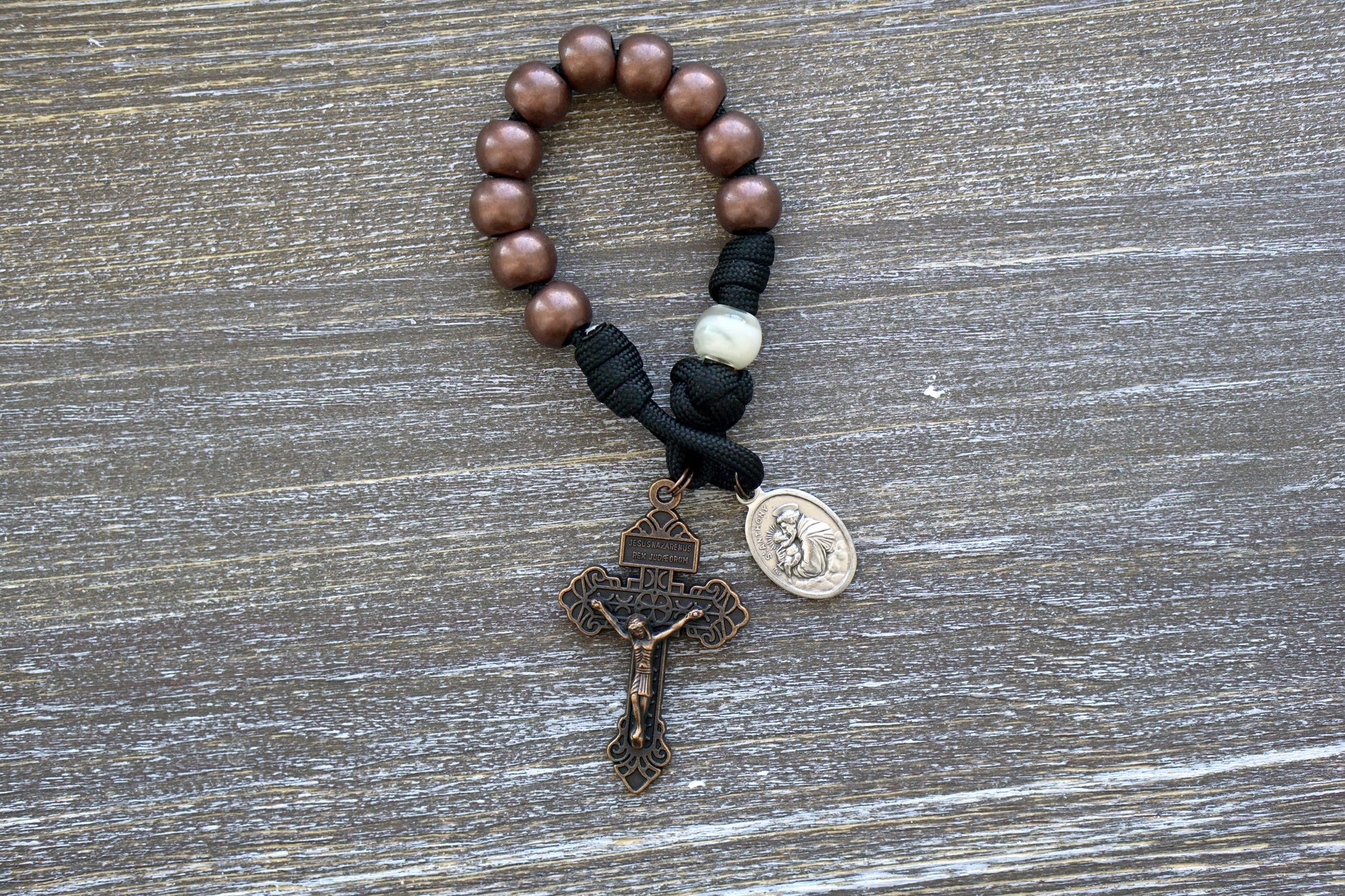 The Heretic Hammer - St. Anthony - Pocket Paracord Rosary, featuring black paracord with copper and pearl beads, St. Anthony devotional medal, and copper Pardon Crucifix for a stylish and meaningful addition to daily prayers, built to withstand daily use and available in full size or single decade version.