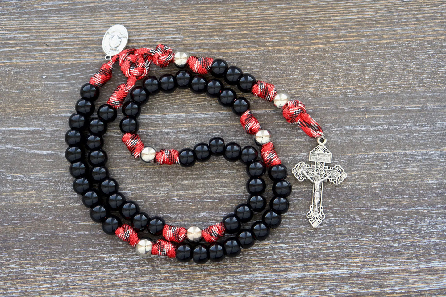 Shiny black paracord beads and silver Our Father beads on a 5-decade rosary, symbol of first responder resilience.