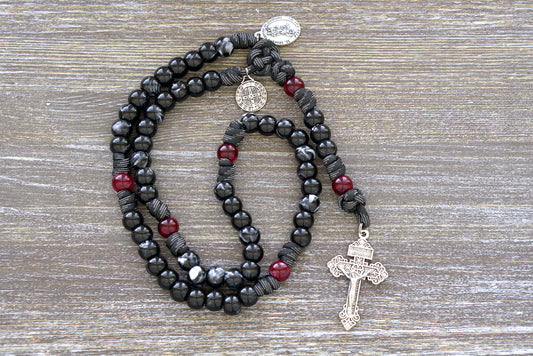 St. Joseph - 5 Decade Black/Red Paracord Rosary, featuring Hail Mary beads in black/white luster and Our Father beads in red/maroon, with a 2" silver pardon crucifix, double devotional medal pairing of St. Joseph and St. Benedict.