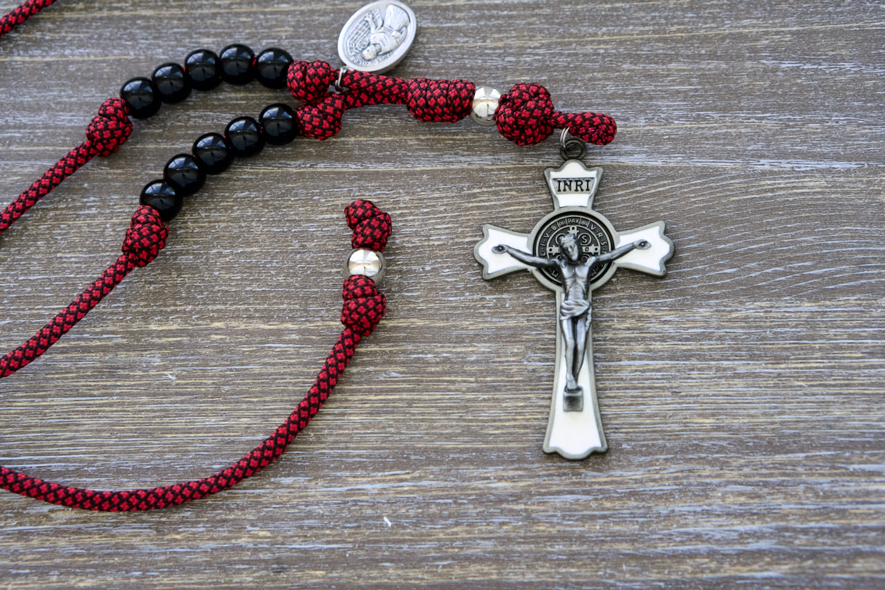 St. Maximilian Kolbe Rearview Mirror Rosary, a compact and powerful red paracord rosary featuring black beads, silver Our Father bead, large white enamel St. Benedict crucifix.