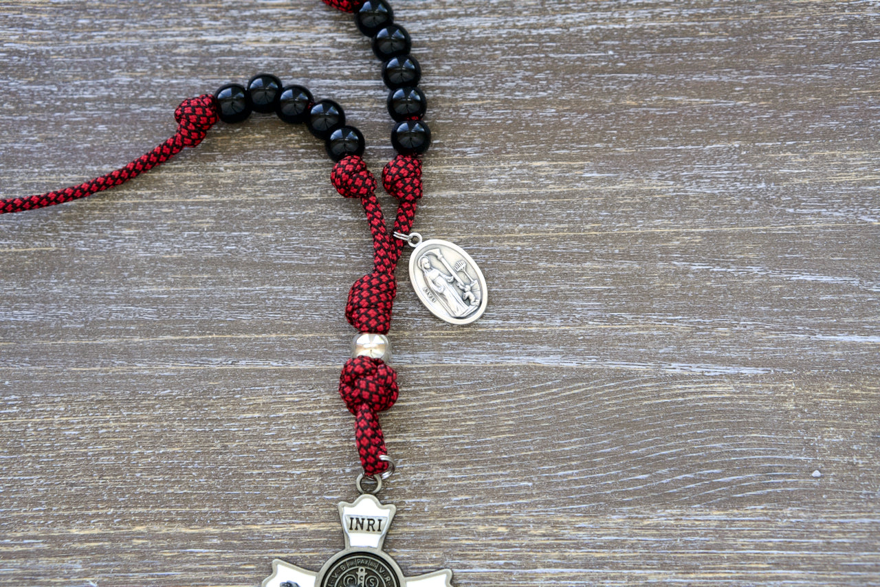 High-quality, compact red paracord rosary with 10 black Hail Mary beads, silver Our Father bead, and large white enamel St. Benedict crucifix for daily travels; includes St. Kolbe devotional medal.