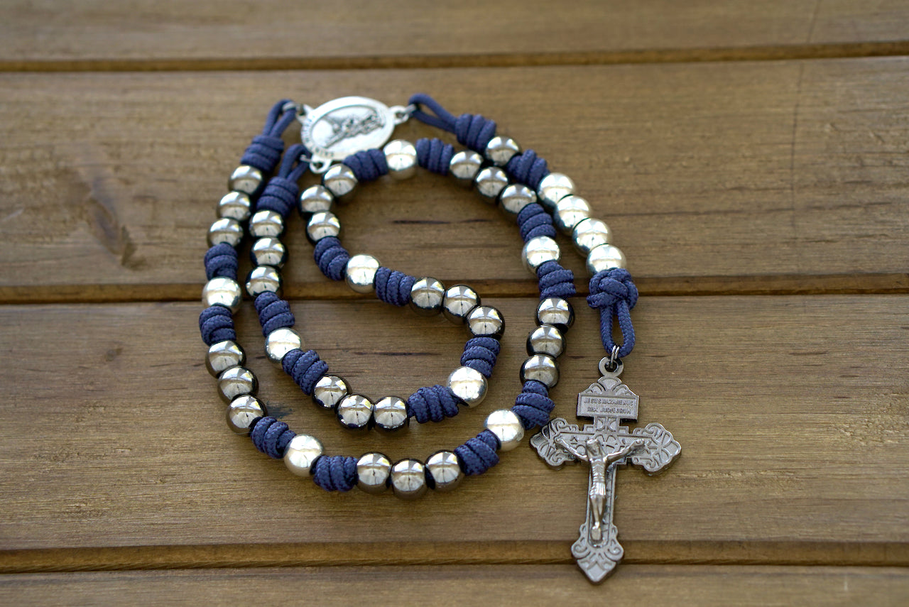 St. Michael Chaplet - Blue and Gunmetal: A premium paracord chaplet featuring navy blue cord, 10mm silver-tone metal beads, a striking St. Michael medal centerpiece, and a Pardon crucifix. Designed for durability and daily Catholic prayer.