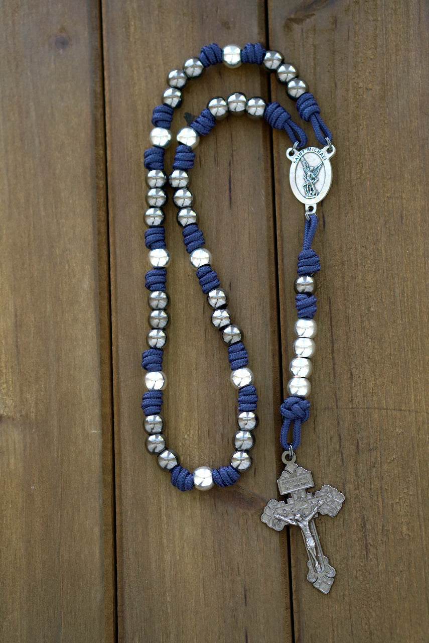 St. Michael Chaplet - Blue and Gunmetal: Close-up image showcasing a navy blue paracord chaplet with silver-toned 10mm metal beads, a prominent St. Michael medal centerpiece, and a 2-inch Pardon crucifix.