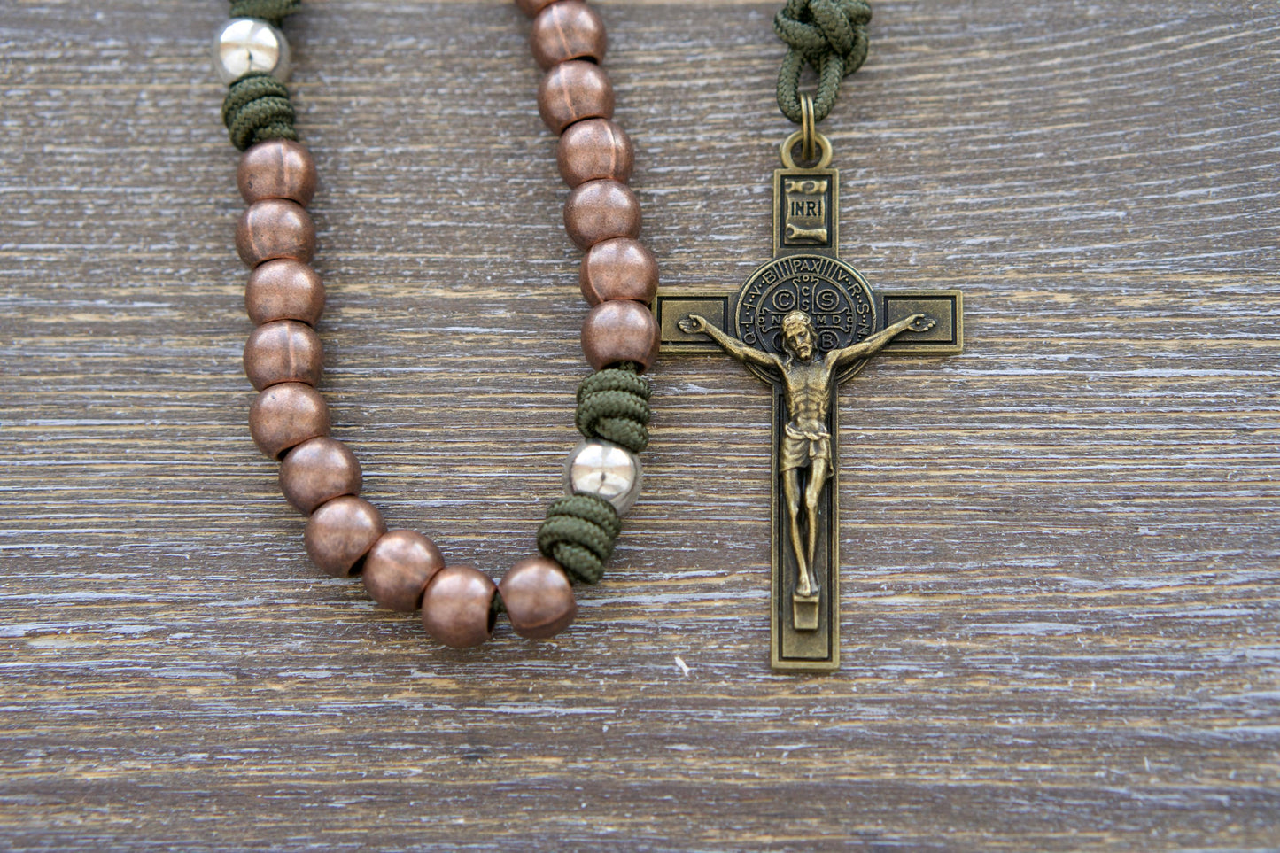 St. Michael's Shield Premium Metal Paracord Rosary: A close-up image showcasing vibrant green paracord interwoven with copper Hail Mary beads and silver Our Father beads, accented by a radiant olive St. Michael centerpiece medal and a 2.5 inch olive St. Benedict crucifix.