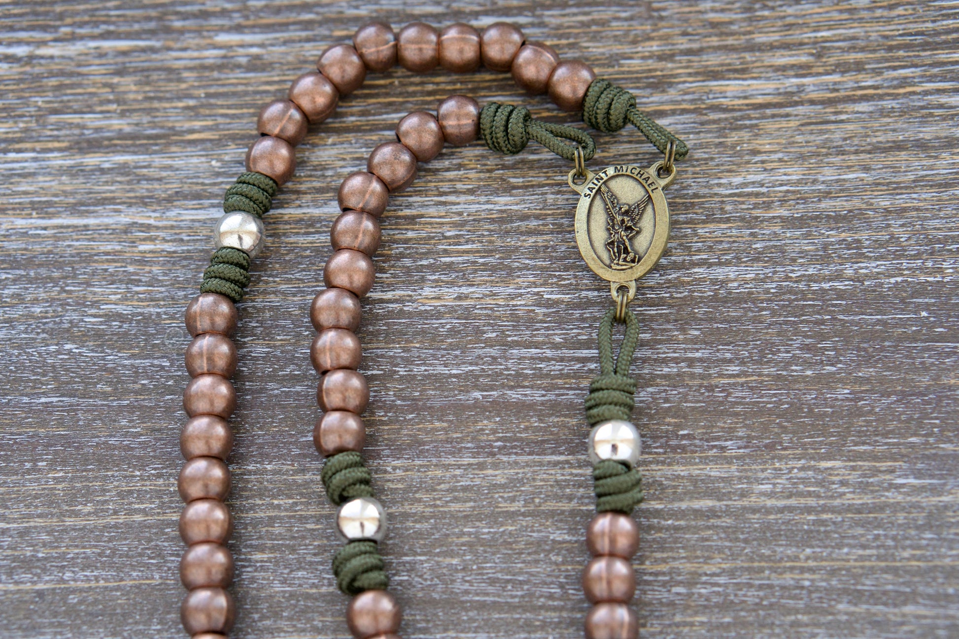 St. Michael's Shield premium paracord rosary featuring green paracord, copper Hail Mary beads, silver Our Father beads, a radiant olive St. Michael centerpiece devotional medal, and an elegant olive St. Benedict crucifix.