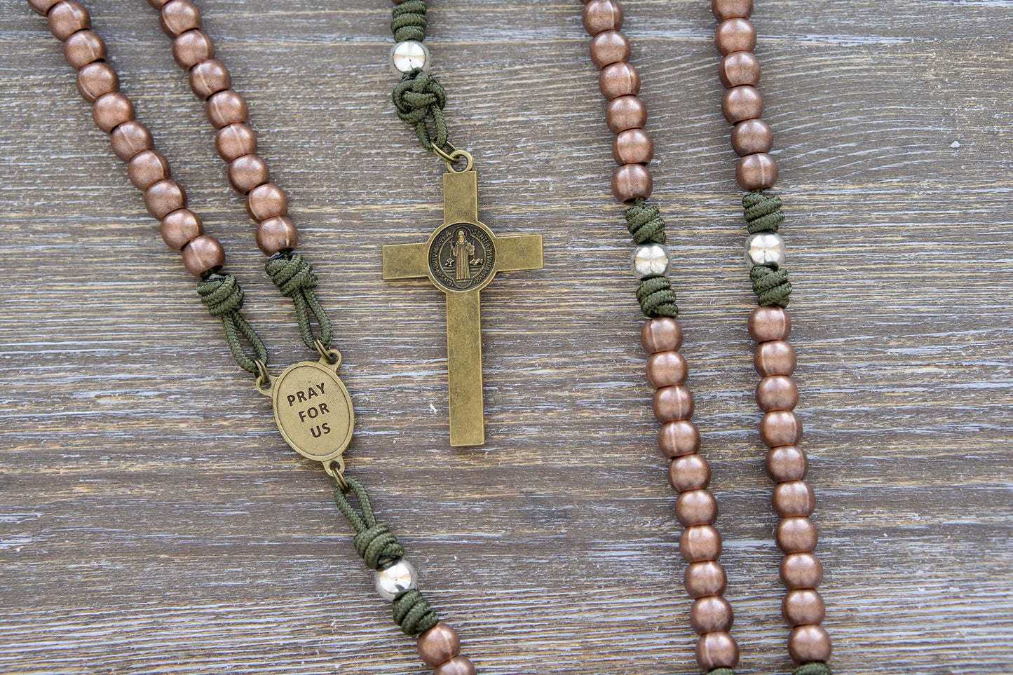 St. Michael's Shield Premium Metal Paracord Rosary: Close-up image showcasing green paracord interwoven with copper Hail Mary beads and silver Our Father beads, featuring a radiant olive St. Michael centerpiece medal and a 2.5 inch olive St. Benedict crucifix.