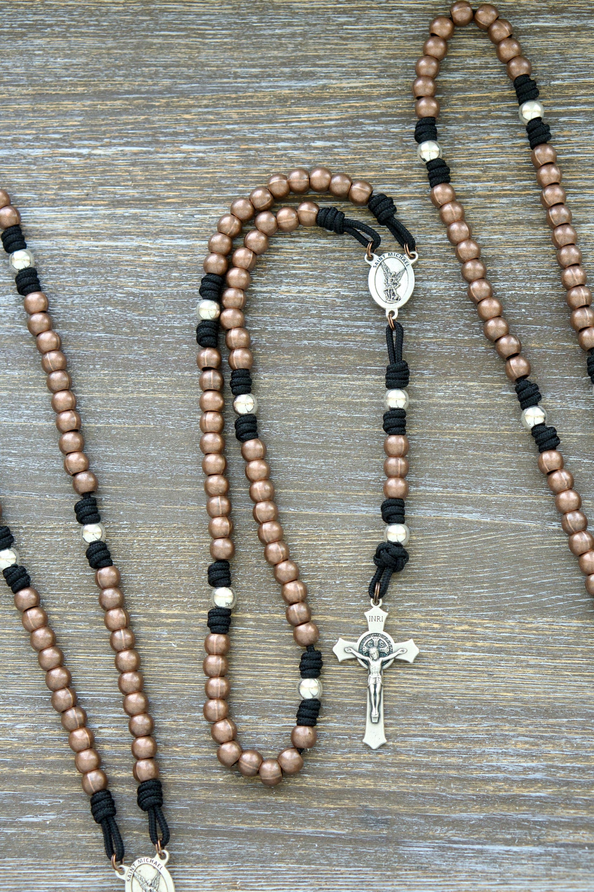 Handcrafted rosary featuring durable paracord (grey, black, green, or navy) with copper Hail Mary beads, silver Our Father beads, a radiant St. Michael centerpiece medal.