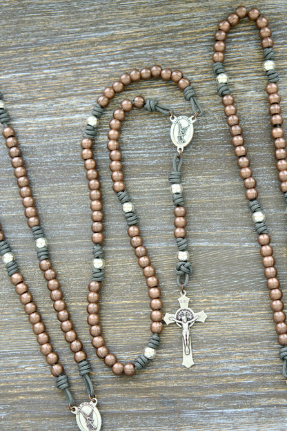 A handcrafted rosary featuring durable paracord (grey, black, green, or navy), silver Our Father beads, copper Hail Mary beads, a radiant St. Michael centerpiece medal, and a 2-inch St. Benedict crucifix.