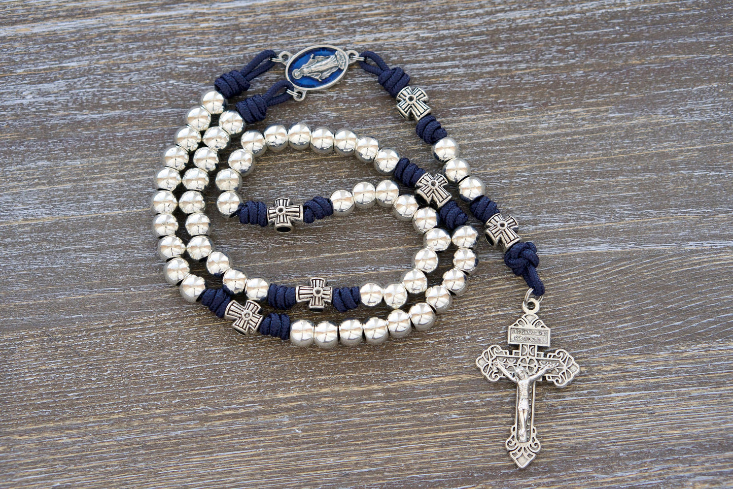 Alt Text:
Navy blue paracord rosary with shimmering silver metal alloy Hail Mary beads, an intricate cross-shaped Our Father bead pattern, a blue enamel Miraculous Medal centerpiece, and a matching silver Pardon Crucifix.  This Stella Maris rosary honors Our Lady, Star of the Sea.