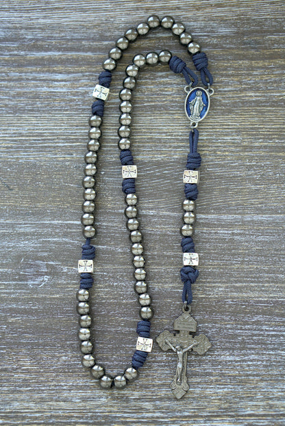 Premium navy blue paracord rosary, "The Solemn Crusader," featuring silver crusader Our Father beads, gunmetal Hail Mary beads, a Miraculous Medal centerpiece, and a 2-inch pardon crucifix. 