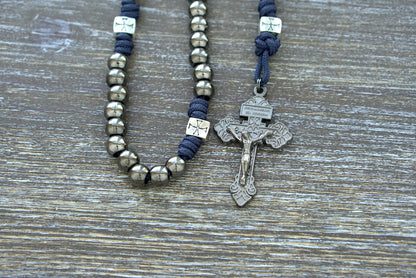 A premium navy blue paracord rosary, "The Solemn Crusader," featuring silver crusader Our Father beads, gunmetal Hail Mary beads, a Miraculous Medal centerpiece, and a 2-inch Pardon crucifix.