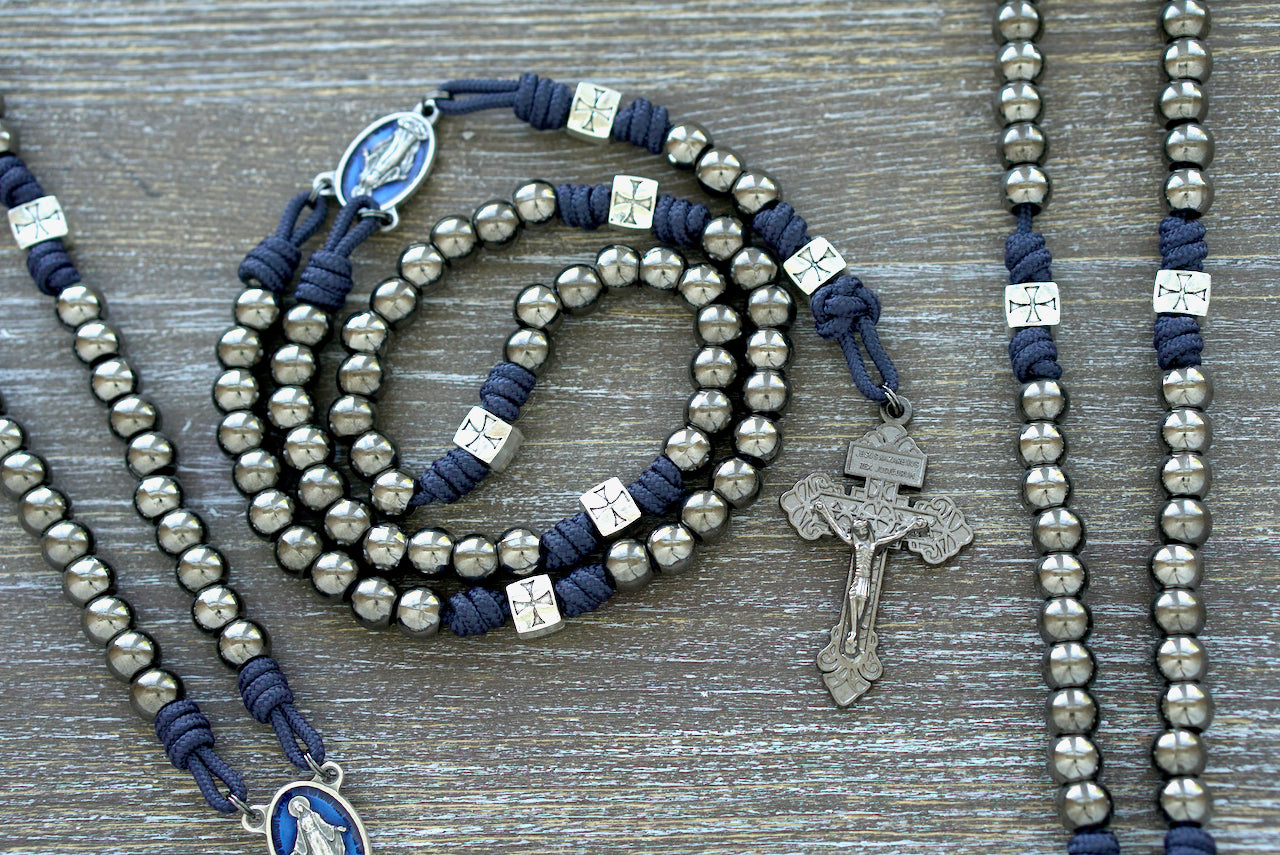 The Solemn Crusader premium paracord rosary, featuring durable navy blue 275 paracord, silver crusader Our Father beads, gunmetal Hail Mary beads, and a blue enamel Miraculous Medal centerpiece. Handcrafted by a Catholic family for spiritual strength and daily prayer.