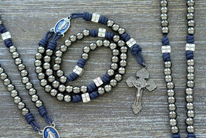 The Solemn Crusader premium paracord rosary, featuring durable navy blue 275 paracord, silver crusader Our Father beads, gunmetal Hail Mary beads, and a blue enamel Miraculous Medal centerpiece. Handcrafted by a Catholic family for spiritual strength and daily prayer.