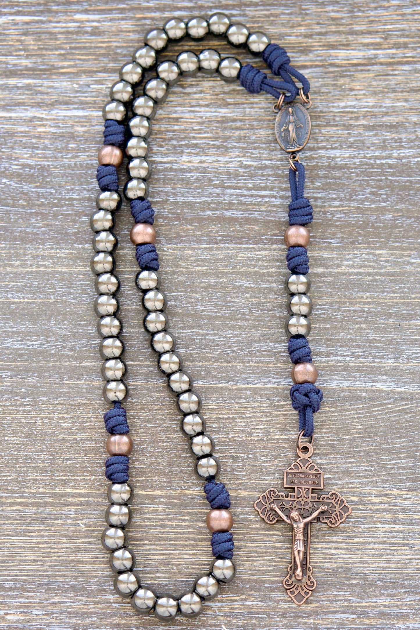 Navy blue paracord rosary featuring antique copper and gunmetal beads, a copper Miraculous Medal centerpiece, and a copper Pardon Crucifix. Handmade with durable materials for everyday wear and prayer.