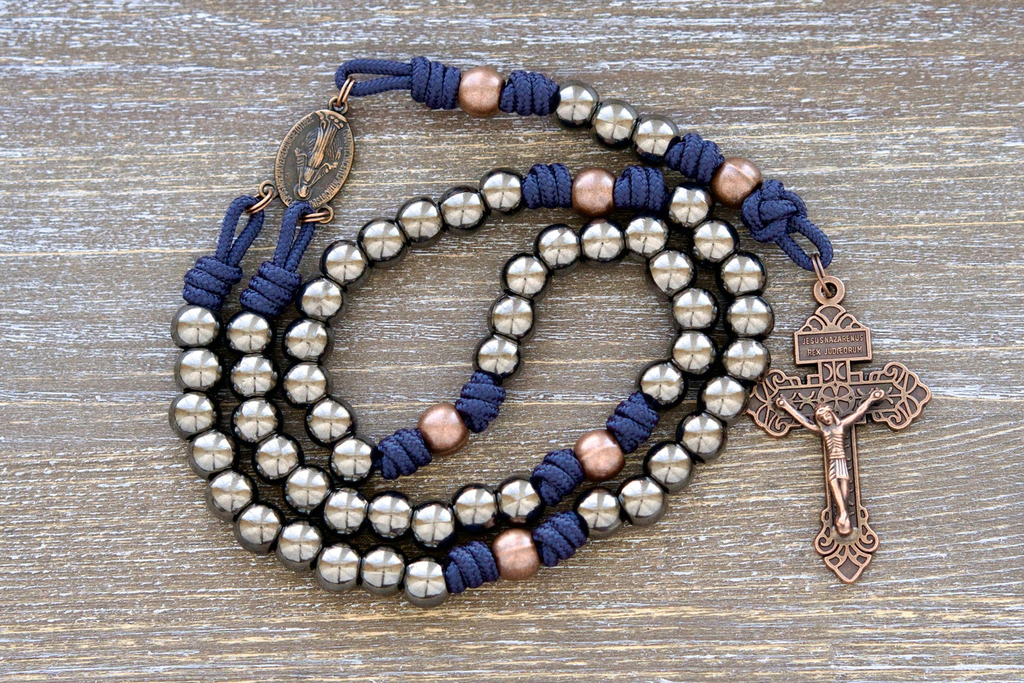 Handmade navy blue paracord rosary featuring 10mm gunmetal Hail Mary beads, antique copper Our Father beads, a copper Miraculous Medal centerpiece, and a 2-inch copper Pardon crucifix.