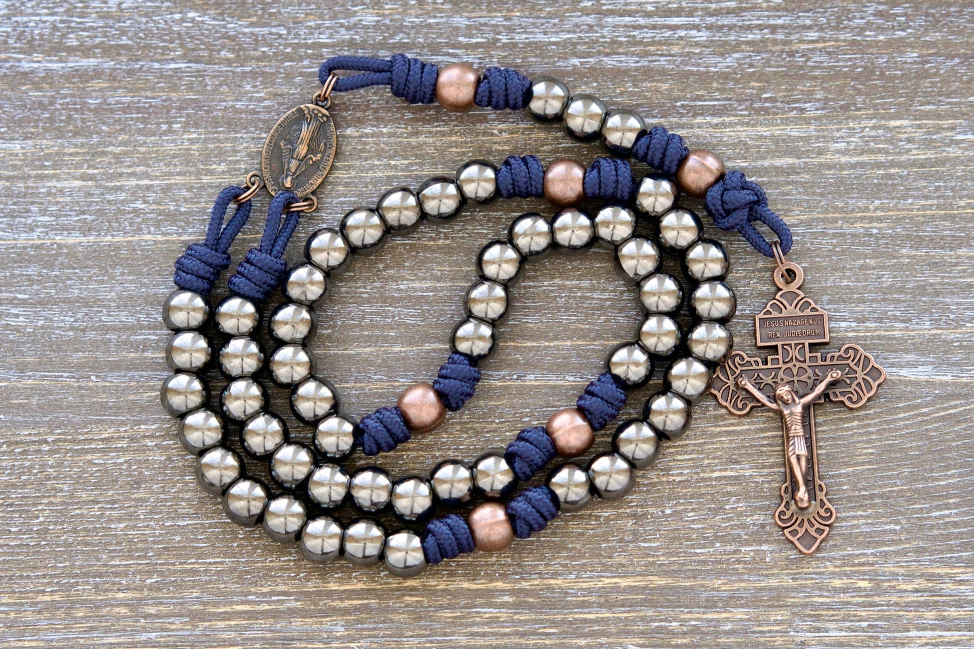 Handmade navy blue paracord rosary featuring 10mm gunmetal Hail Mary beads, antique copper Our Father beads, a copper Miraculous Medal centerpiece, and a 2-inch copper Pardon crucifix.