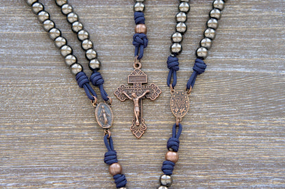 Unbreakable Fidelity premium metal paracord rosary featuring navy blue paracord, 10mm gunmetal Hail Mary beads, antique copper Our Father beads, a copper Miraculous Medal centerpiece, and a 2-inch copper Pardon Crucifix.