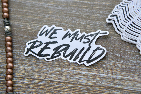 We Must Rebuild vinyl sticker, 4.25" x 2.13", features a bold call to action for rebuilding faith, society, and families, inspired by Isaiah 61:4.  Waterproof, removable white vinyl with matte lamination for durability and indoor/outdoor use.