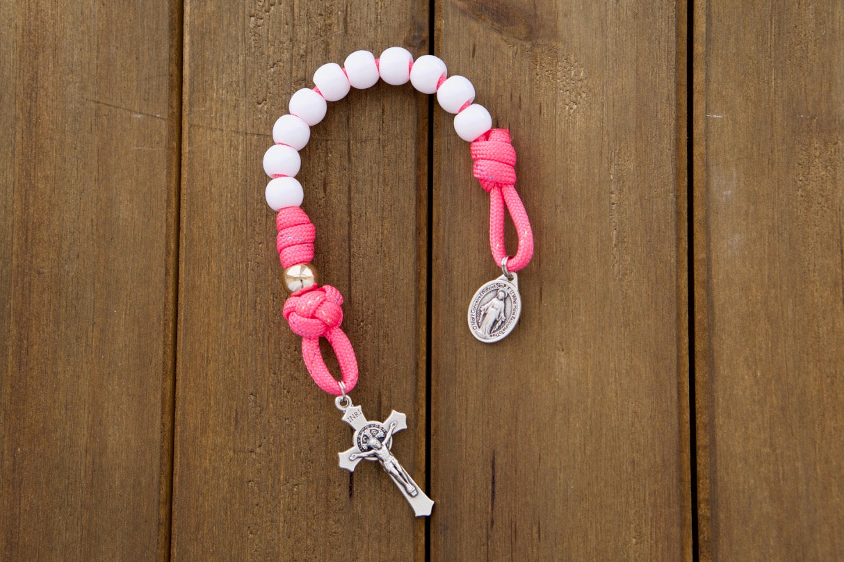 A beautiful Kid's pink pocket paracord rosary with white Hail Mary beads and rose gold Our Father beads, perfect for children learning to pray the rosary. Durable and unbreakable paracord 550 with smaller 10mm beads, an ideal Easter or First Communion gift, along with a St. Benedict Crucifix and Miraculous Medal.