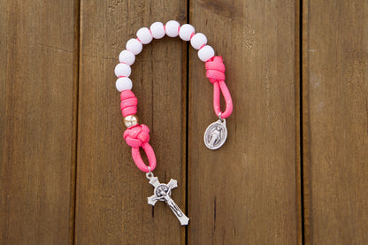A beautiful Kid's pink pocket paracord rosary with white Hail Mary beads and rose gold Our Father beads, perfect for children learning to pray the rosary. Durable and unbreakable paracord 550 with smaller 10mm beads, an ideal Easter or First Communion gift, along with a St. Benedict Crucifix and Miraculous Medal.