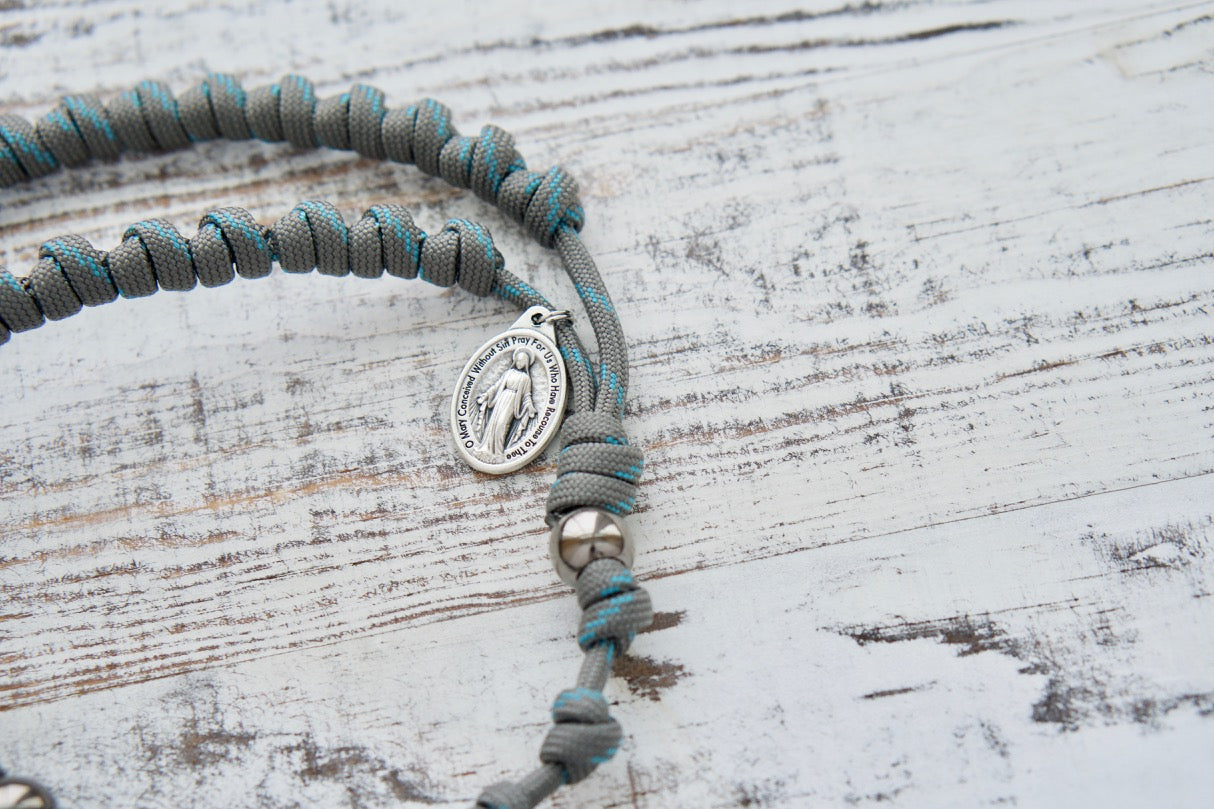 Heaven's Embrace - Grey, Teal Blue, Gunmetal - Knotted Rope Rosary by Sanctus Servo. This durable, premium, unbreakable paracord rosary is designed with a grey and gunmetal color scheme and features acrylic accent beads for a traditional Catholic look.