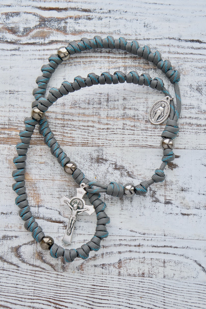 Heaven's Embrace - Grey, Teal Blue, Gunmetal Knotted Rope Rosary: A premium, unbreakable paracord rosary designed for spiritual protection. Durable and tested by kids, it features a grey and gunmetal design with acrylic accent beads, St. Benedict Crucifix, and Miraculous Medal.