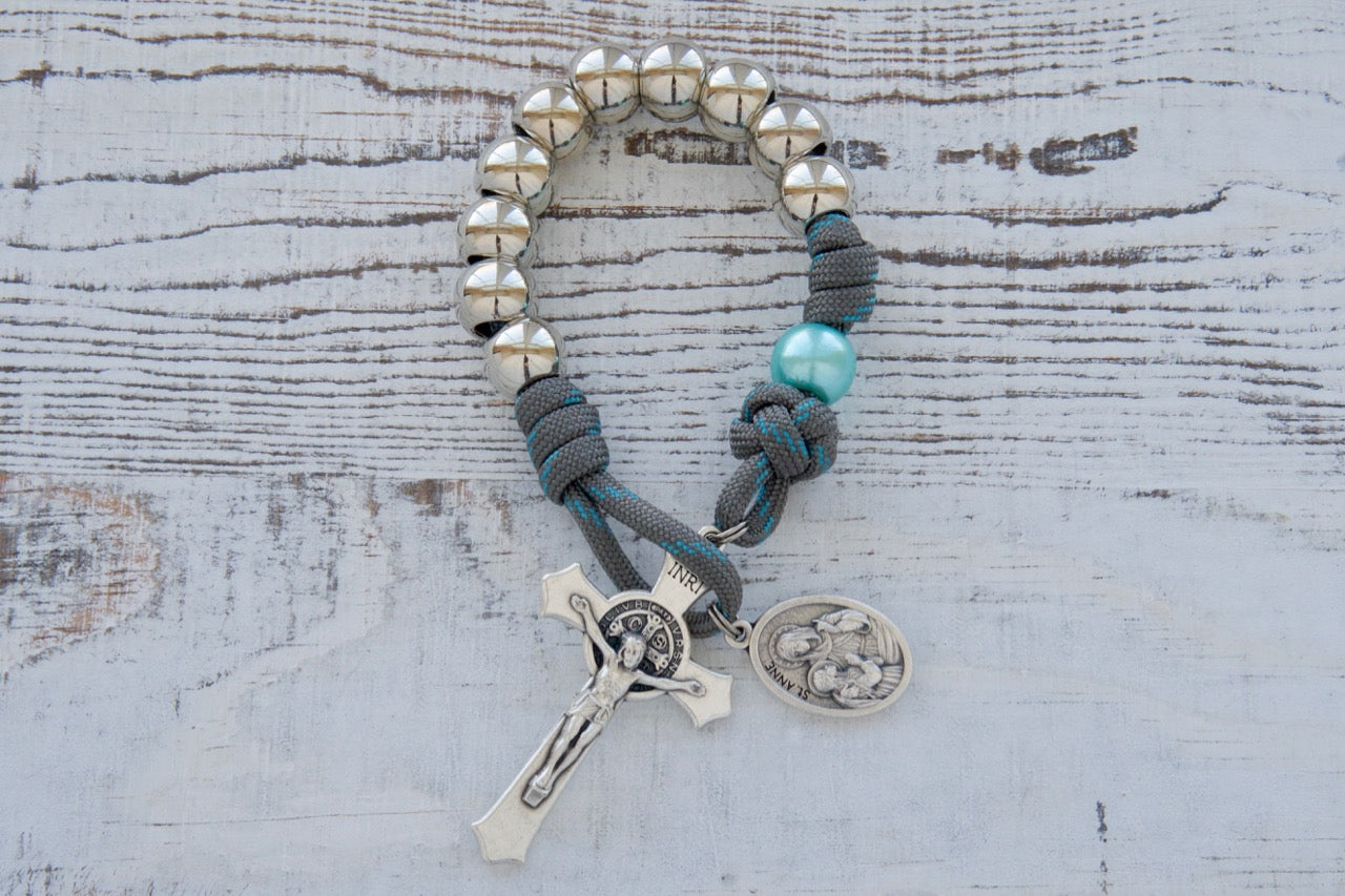 A stunning gray and blue paracord rosary dedicated to St. Anne's Intercession. The rosary features durable, unbreakable paracord rope, silver Hail Mary beads, and sky blue Our Father beads. A beautiful devotional St. Anne medal completes the set, making it an ideal spiritual weapon for any Catholic seeking the intercession of this beloved saint.