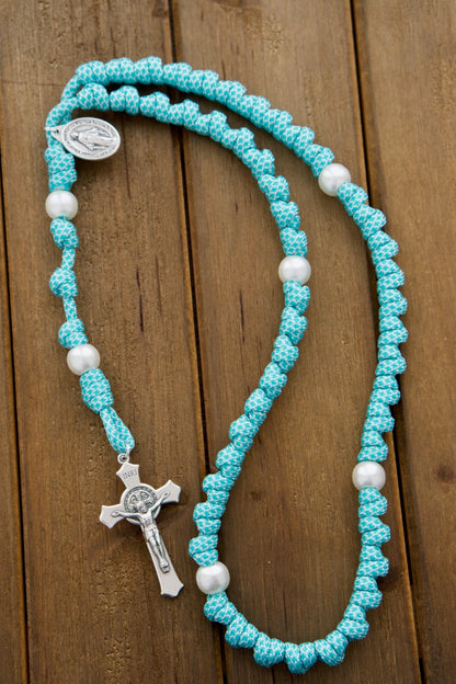 The Peaceful Waters - Teal Blue and White Knotted Rope Rosary, featuring durable Paracord 550 rope, white pearl Our Father beads, a standard 2" St. Benedict Crucifix, and a Miraculous Medal. Perfect for young Catholics or those on the go, join us in prayer with this reliable spiritual weapon. Handmade by our small Catholic family of 6.
