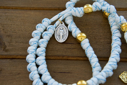 Unshakable Faith - White, Blue and Gold Rope Rosary" - Sanctus Servo's premium unbreakable paracord rosary for Catholics, featuring white and blue durable paracord 550 rope, gold Our Father beads, standard size 2" Gold Pardon Crucifix, Miraculous Medal, and a full-size length of 19 inches. Perfect Catholic gift for your spiritual journey!